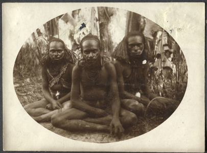 229248 Drie mannen van de Marind-anim zitten in kleermakerszit aan de rand van het bos